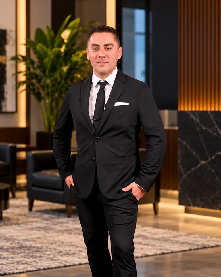 Professor Manny Galvan in a black suit and tie, standing in a modern lobby